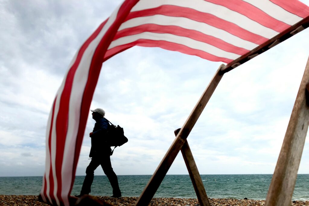A person with a backpack walking under a red and white striped canopy, symbolizing US to Canada migration and identity crisis."